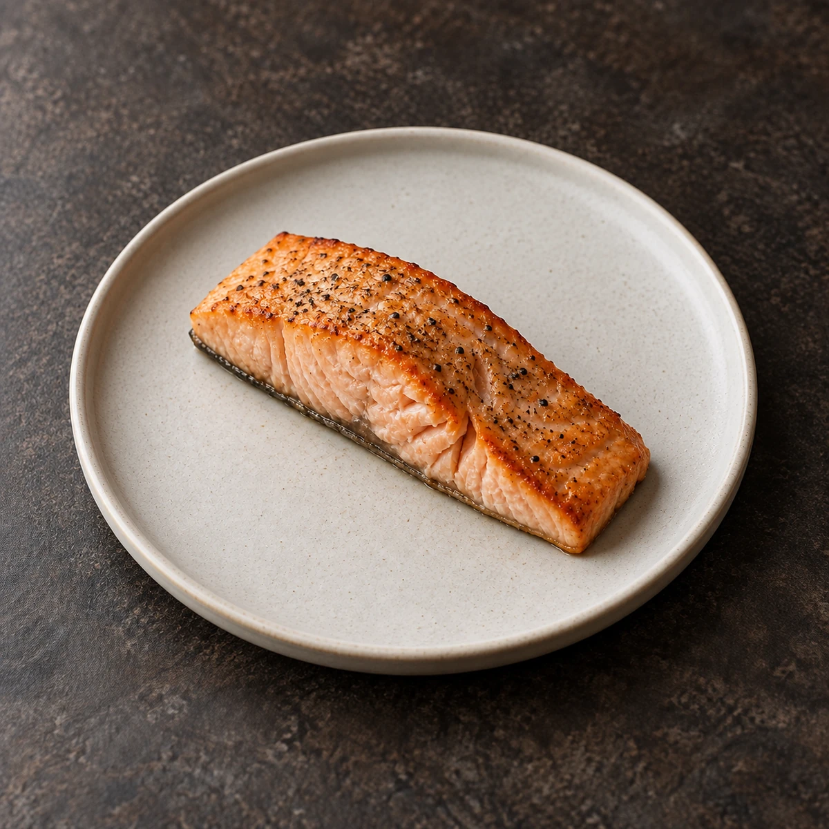 An oven-baked salmon fillet with black pepper on a pale plate